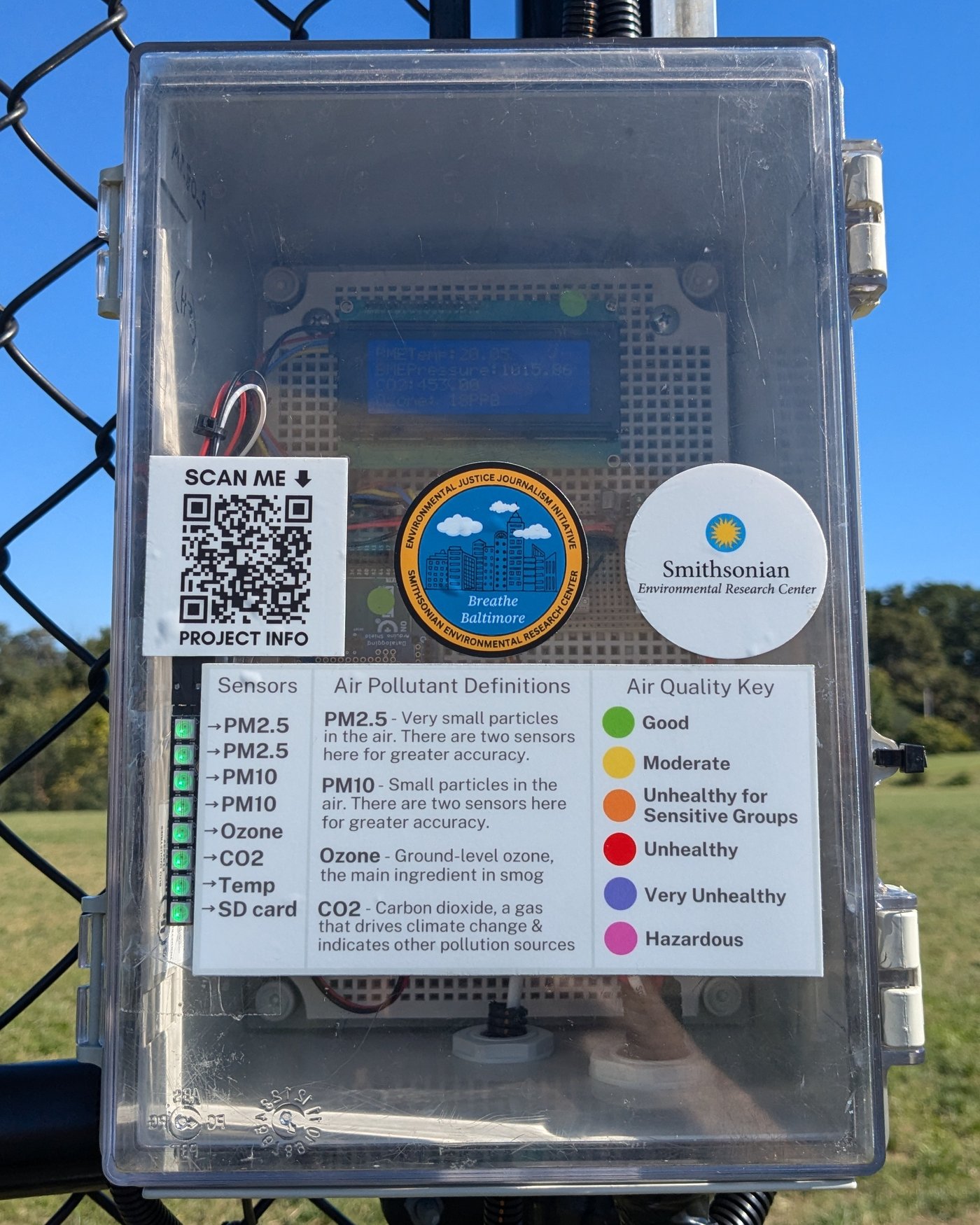 A low-cost air quality sensor deployed in the field, mounted on a fence in a Baltimore park.